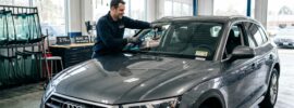 Auto glass technician installing a new windshield on a car with urethane adhesive, ensuring safe drive-away time.