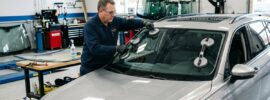 Auto glass technician doing in-shop windshield replacement on a car next to a mobile repair service van.